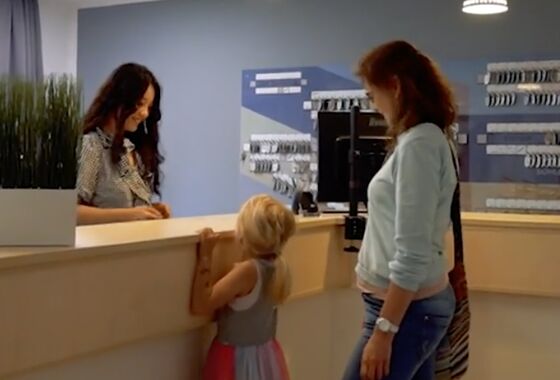 Foto der Empfangstheke mit einer Mitarbeiterin und zwei Gästen