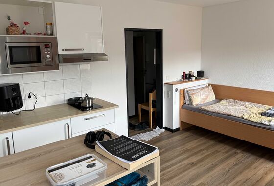 Apartment mit Küchenzeile, Küchengeräten und daneben ein Einzelbett