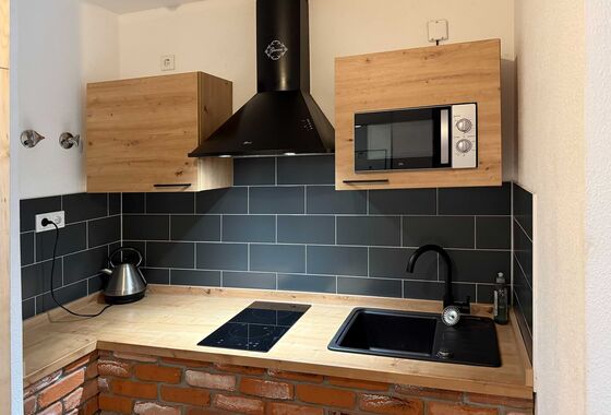 Küchenzeile mit Herd, Dunstabzugshaube, Mikrowelle, Waschbecken und Wasserkocher